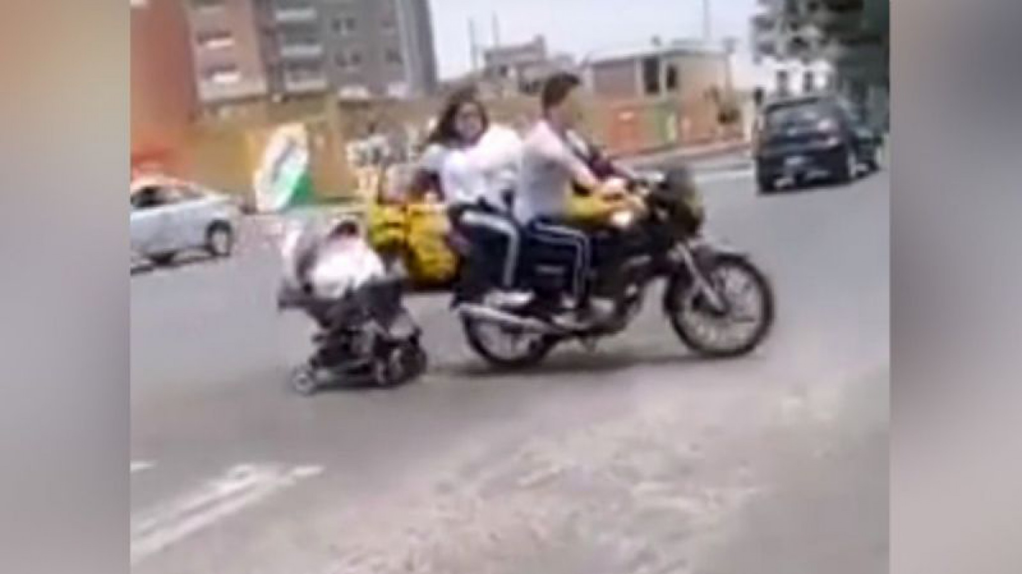 Una locura: Una pareja tira de un cochecito mientras transitan en moto